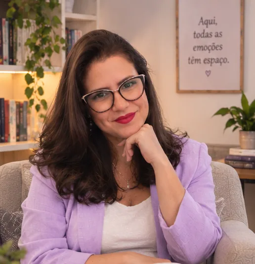 Ludymila Leal sentada em uma poltrona, vestindo terno lilás, escrevendo em um caderno, em ambiente acolhedor